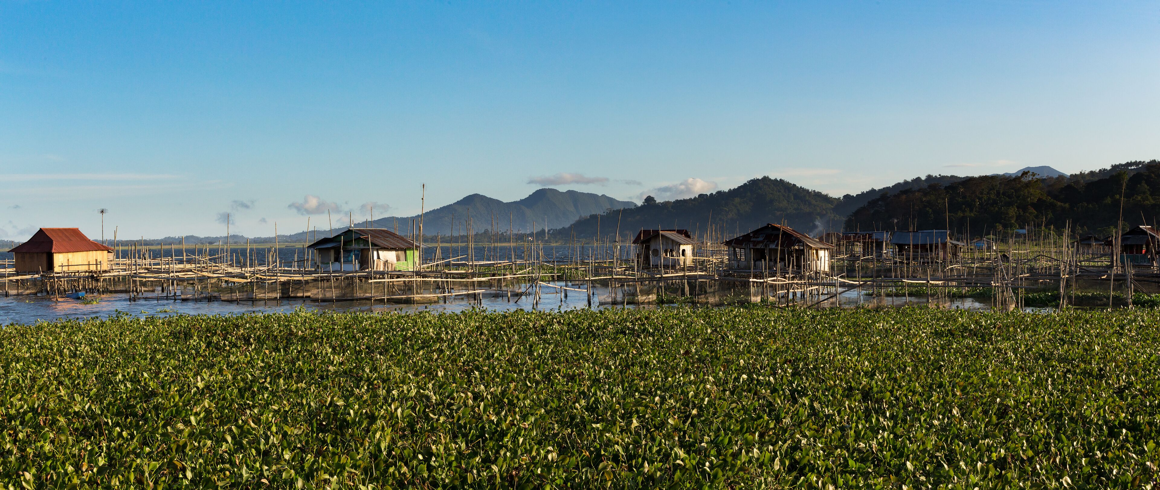 Floating houses on stilts over a water body with a mountainous background.