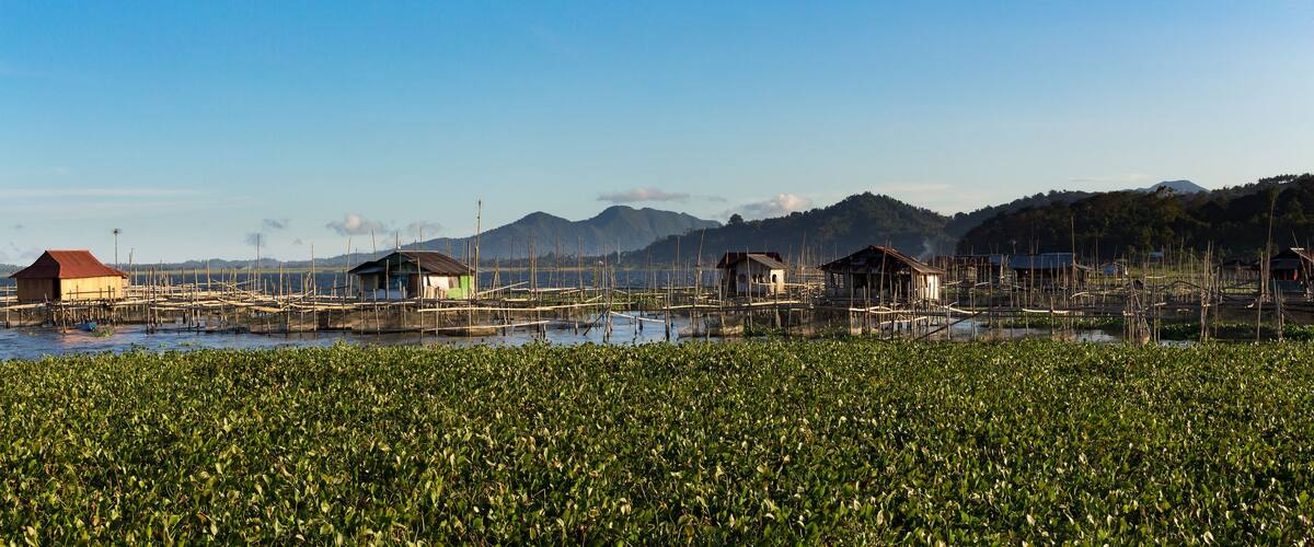 Floating houses on stilts over a water body with a mountainous background.