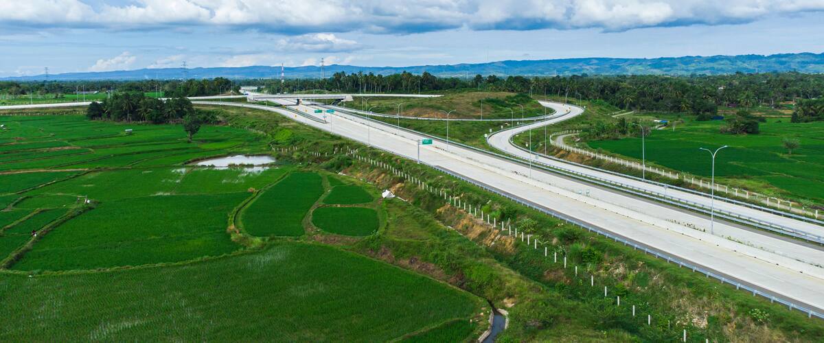 A highway curving through green fields with distant mountains and a cloudy sky.