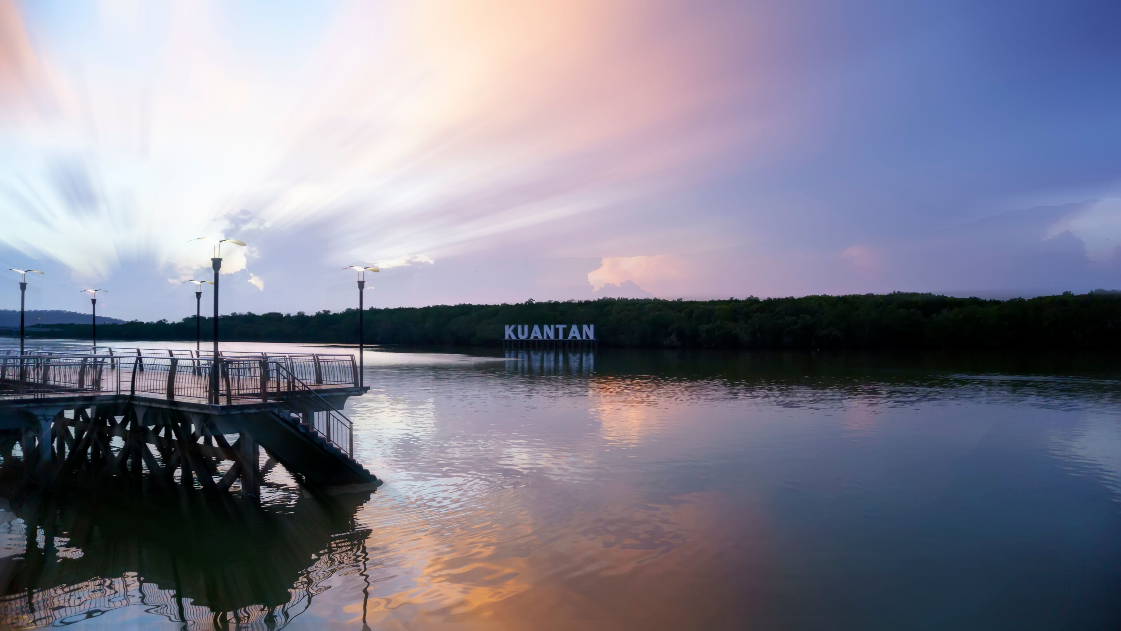 A pier extending into a calm body of water with a sign reading "KUANTAN" in the background.