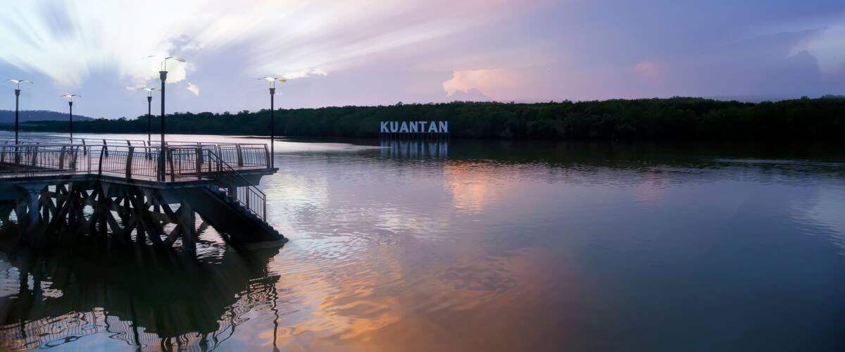A pier extending into a calm body of water with a sign reading "KUANTAN" in the background.