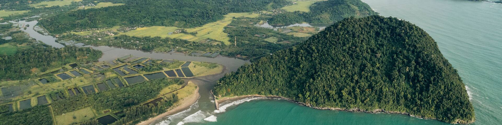 Aerial view of lush green landscape with a prominent coastal hill and vast ocean backdrop. Aceh Jaya Regency, Aceh, Sumatra, Indonesia