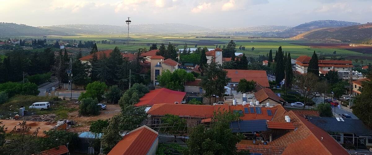 A rural landscape with houses, a church, and rolling hills in the background.