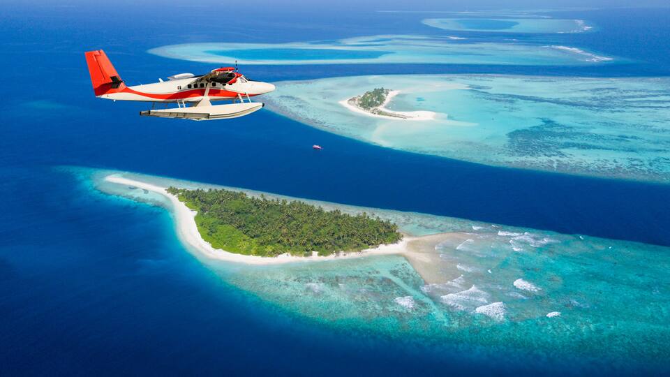 An airplane flying over a chain of turquoise islands with clear blue waters.
