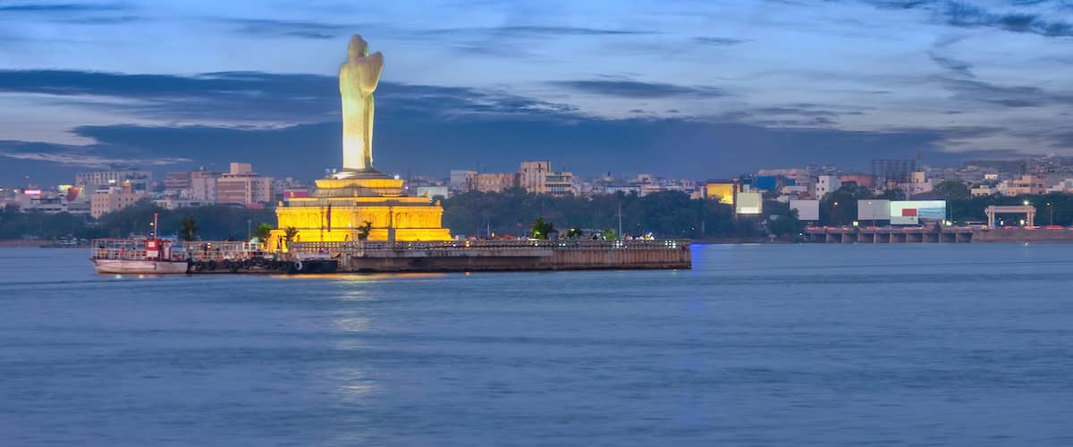 A large golden statue on an island in the middle of a river, with a cityscape in the background.