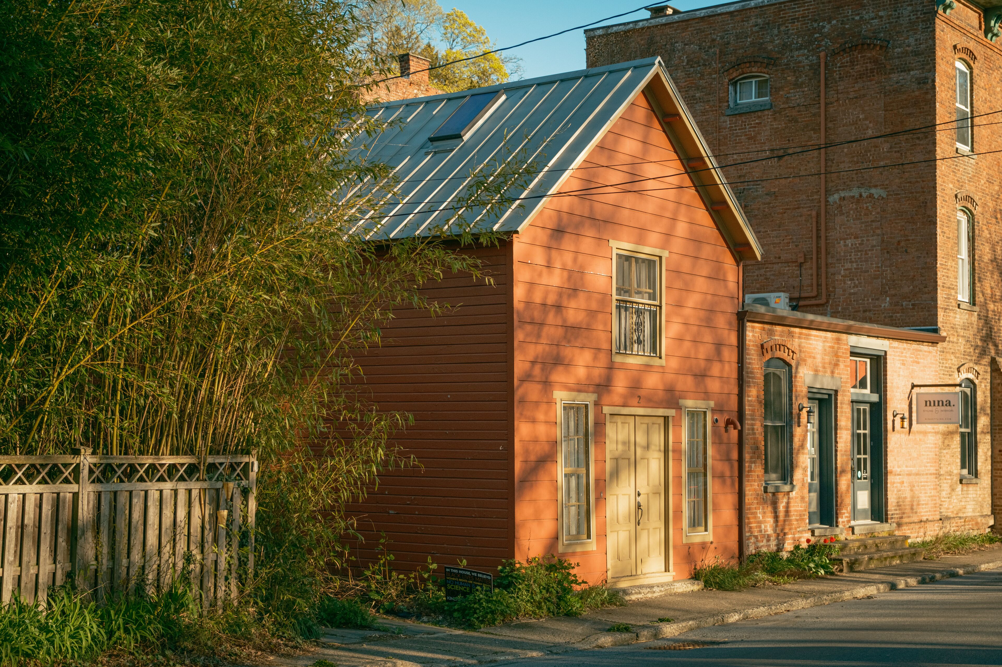 A red wooden building with solar panels, a wooden fence, and a brick building in the background.