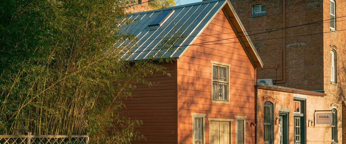 A red wooden building with solar panels, a wooden fence, and a brick building in the background.