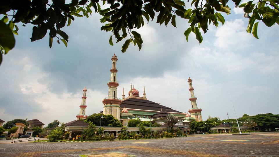A mosque with multiple minarets and domes, surrounded by greenery and a paved courtyard.