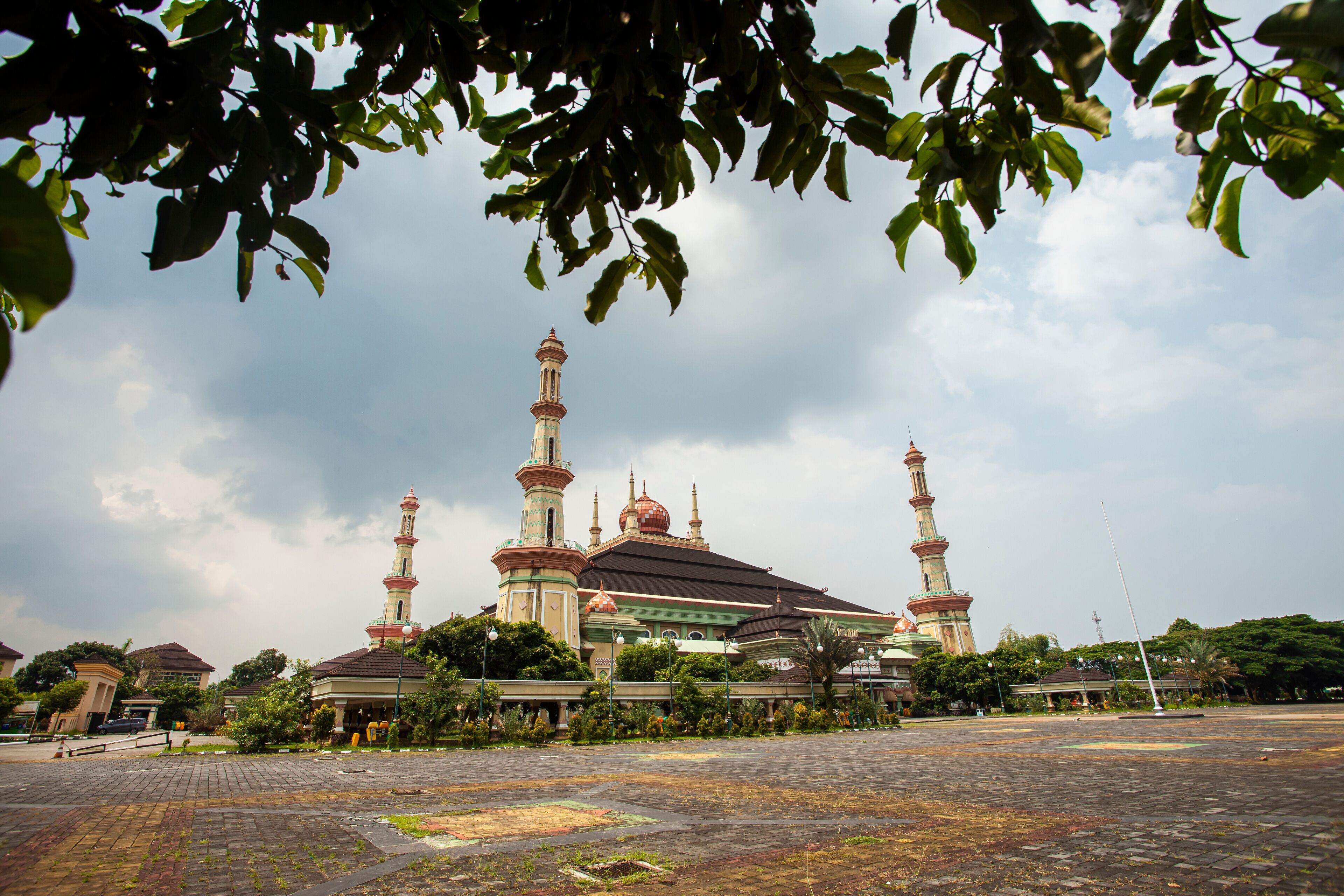 A mosque with multiple minarets and domes, surrounded by greenery and a paved courtyard.