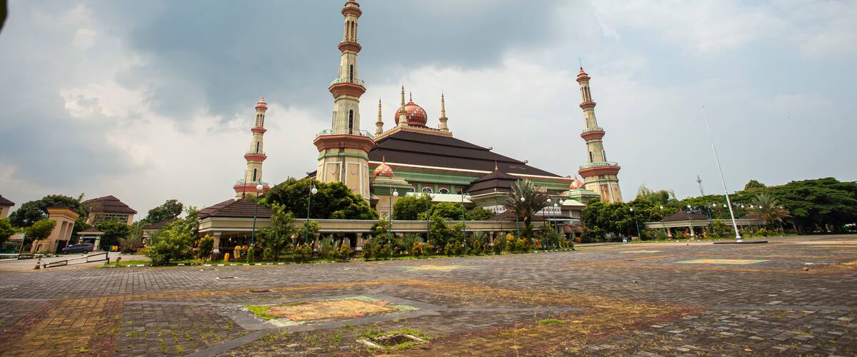 A mosque with multiple minarets and domes, surrounded by greenery and a paved courtyard.