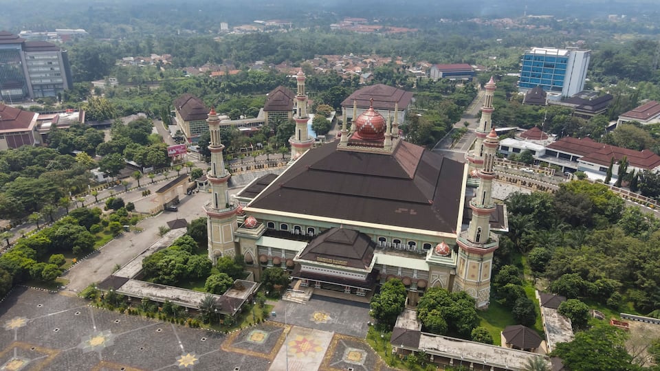 An aerial view of a historic building with a large dome and two minarets, surrounded by lush greenery and urban buildings.