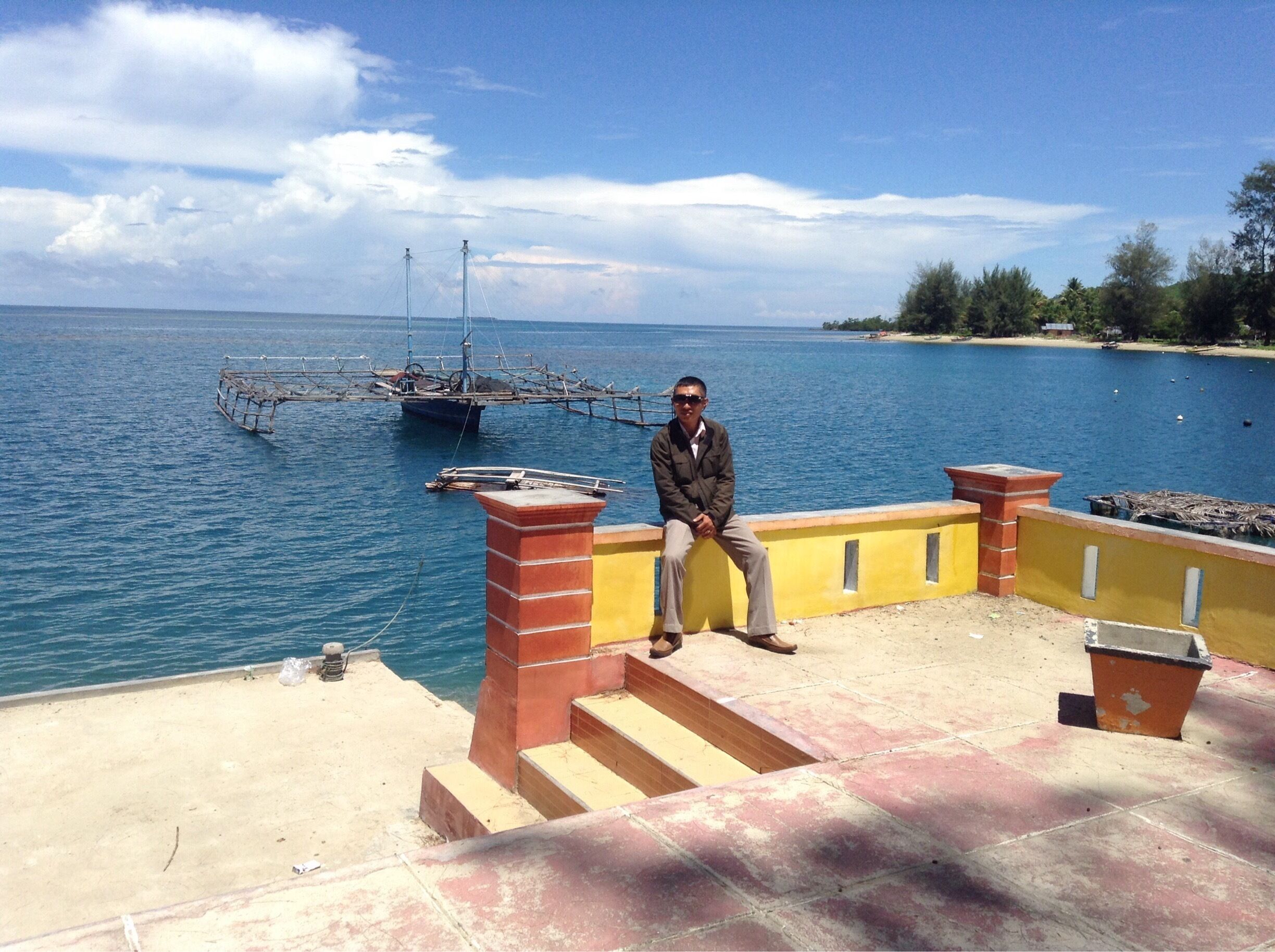 A man sitting on a staircase overlooking a body of water with boats and a distant shoreline.