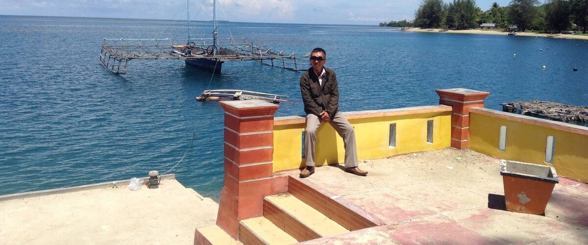 A man sitting on a staircase overlooking a body of water with boats and a distant shoreline.