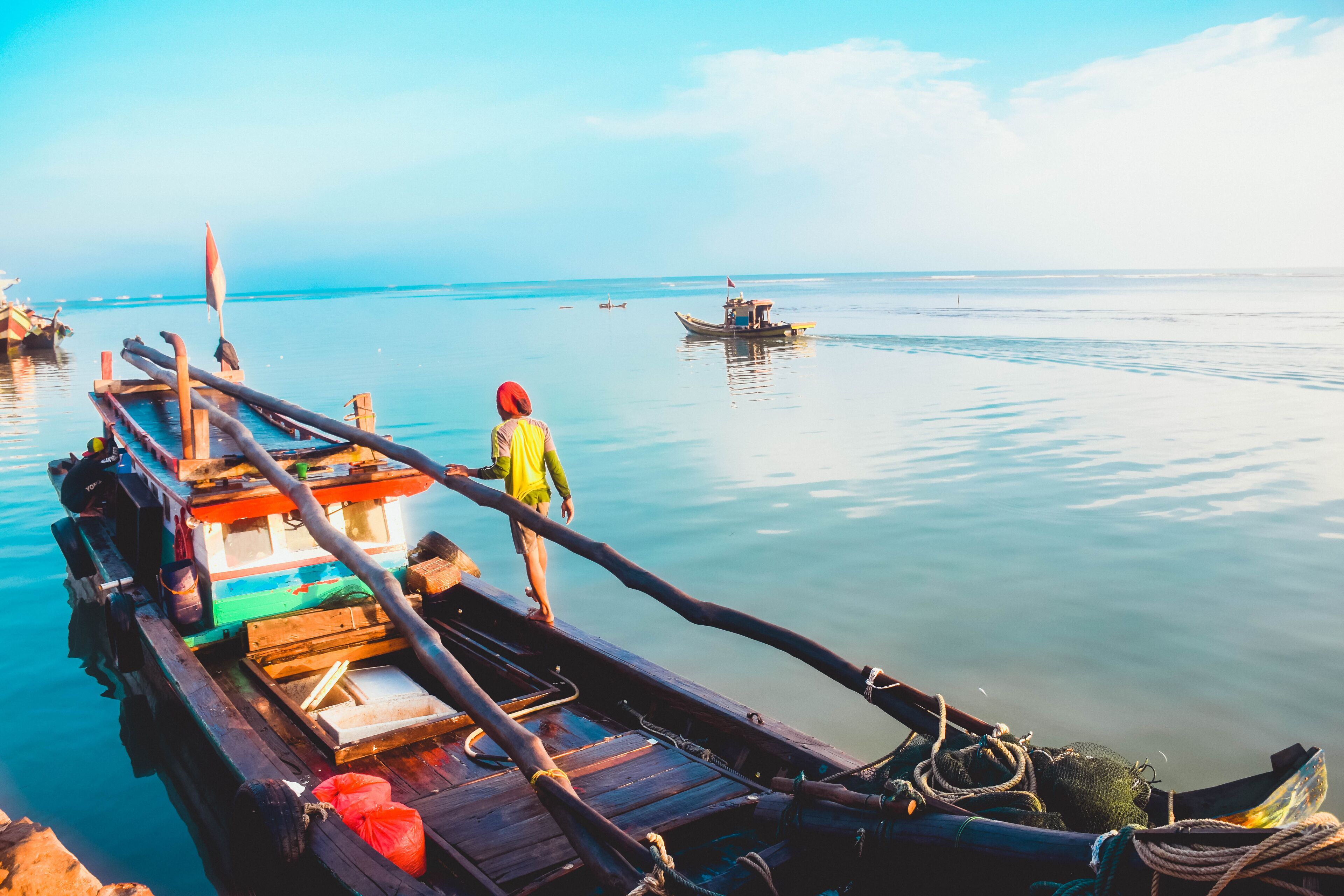 A wooden boat docked at a calm body of water with a person standing on the deck.