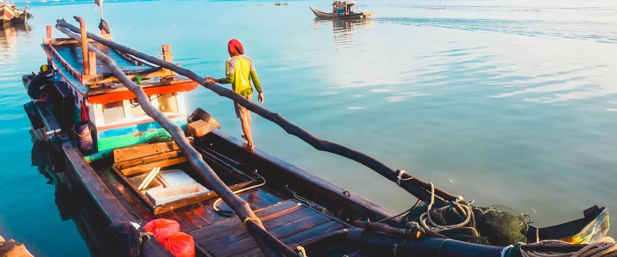 A wooden boat docked at a calm body of water with a person standing on the deck.