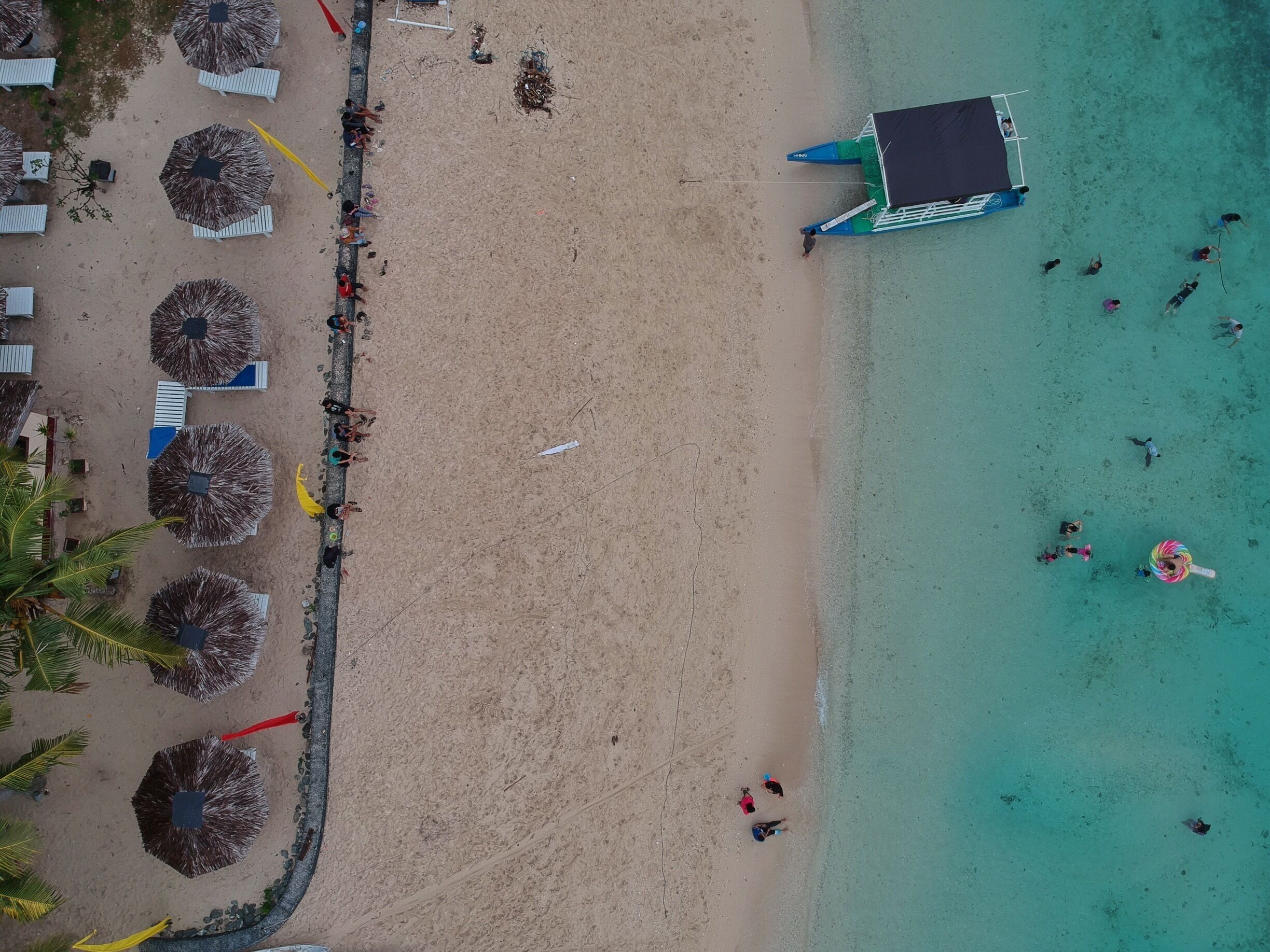 An aerial view of a beach with umbrellas, lounge chairs, and a boat.