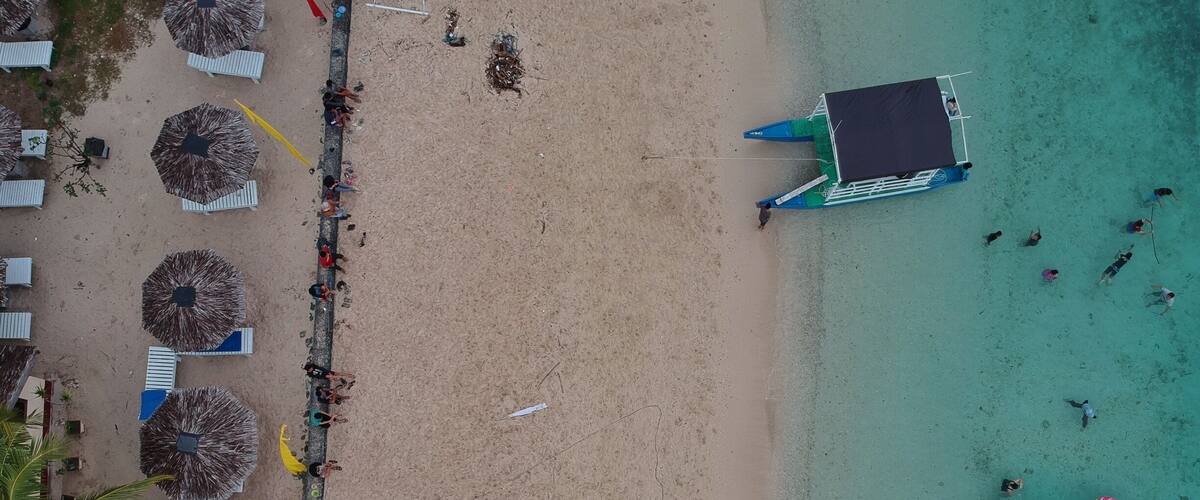 An aerial view of a beach with umbrellas, lounge chairs, and a boat.