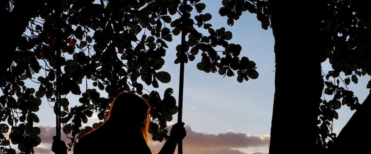 A silhouette of a person on a swing overlooking a sunset over the ocean.