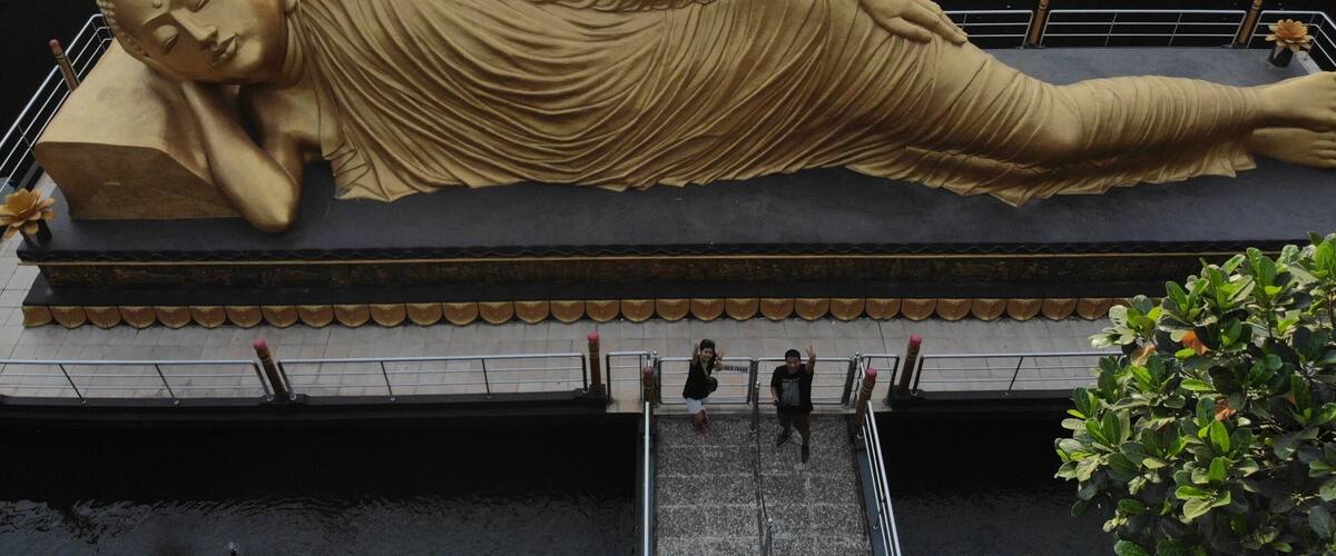 A large reclining Buddha statue on a platform by a body of water.