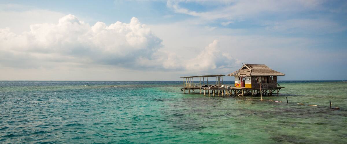 A wooden structure on stilts over clear turquoise water, with a cloudy sky above.