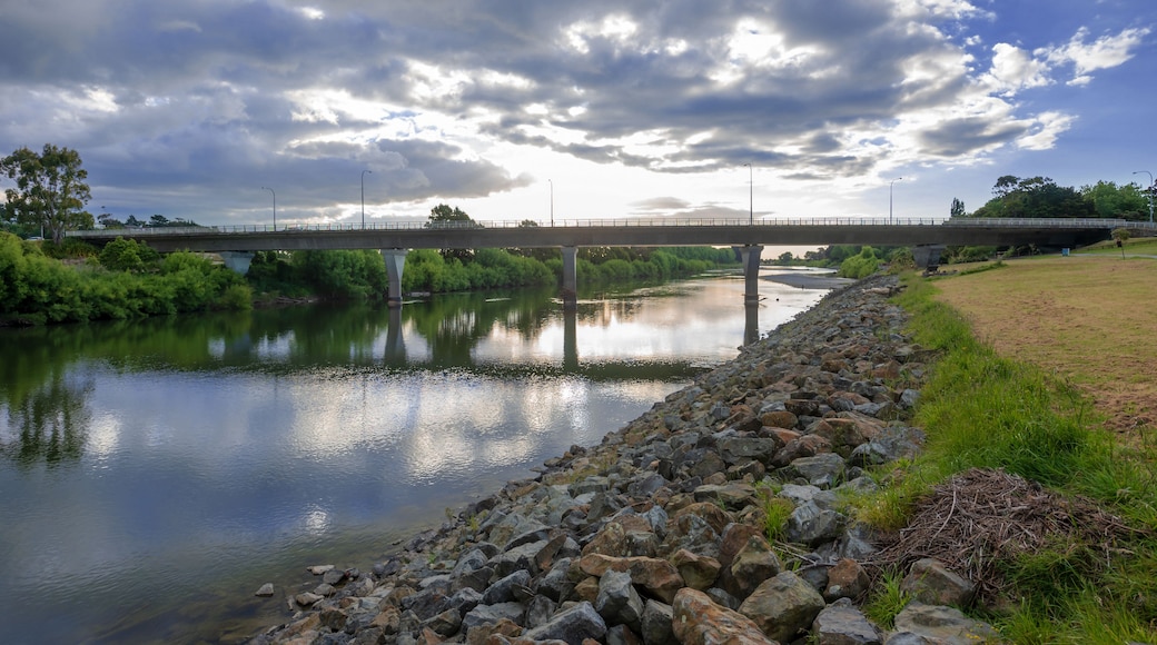 A river with a rocky embankment, a bridge, and a cloudy sky.