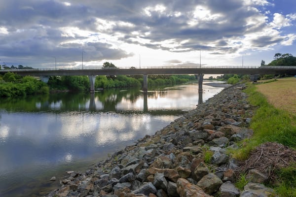 Une rivière aux berges rocheuses, un pont et un ciel nuageux.