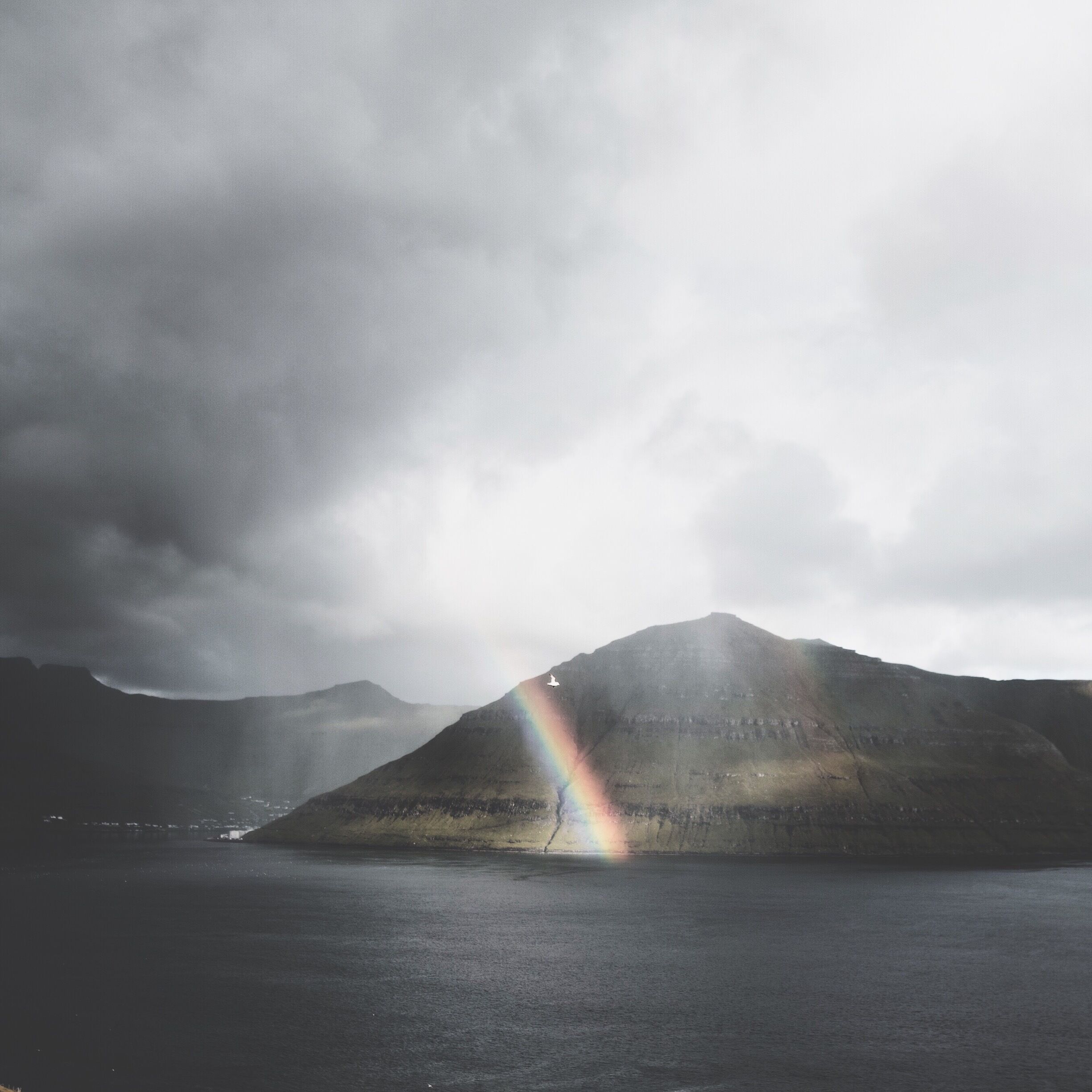 A mountain with a rainbow over a body of water.