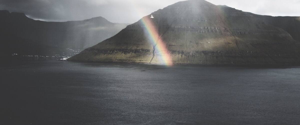 A mountain with a rainbow over a body of water.