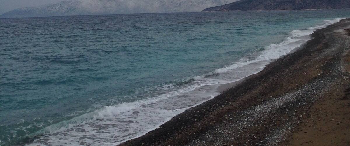 A beach with a rocky shoreline and distant snow-capped mountains under a cloudy sky.