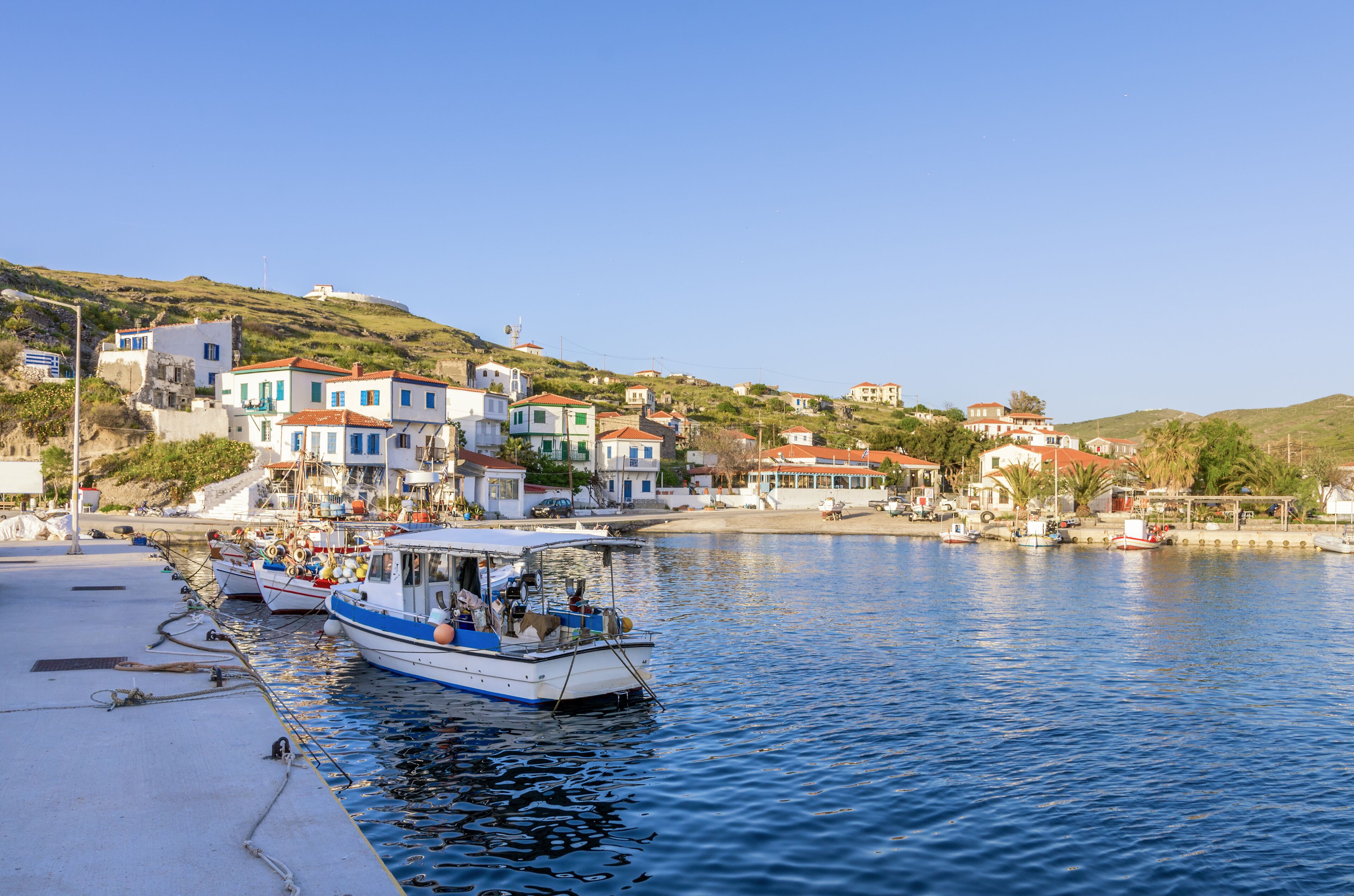 A coastal village with boats docked at a pier, surrounded by colorful houses and hills.