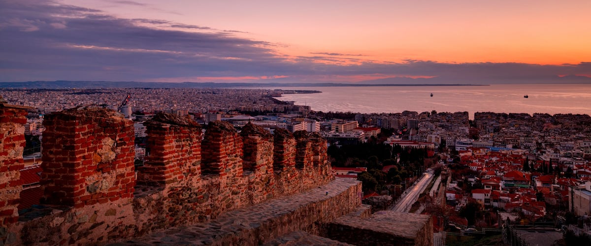 A sunset over a coastal city with historic fortifications and a view of the sea.