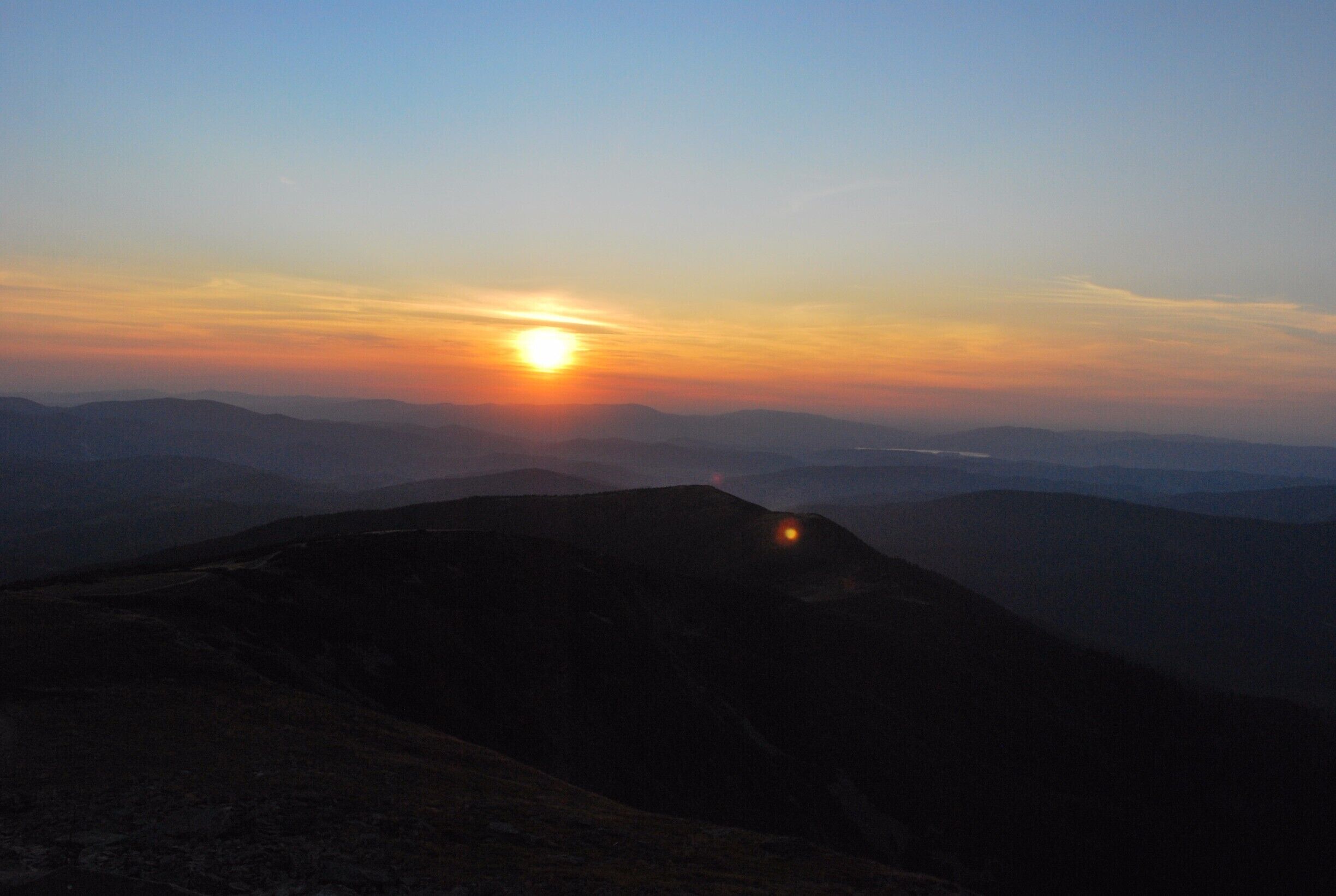 A sunset over a mountainous landscape with a visible light source on a hill.