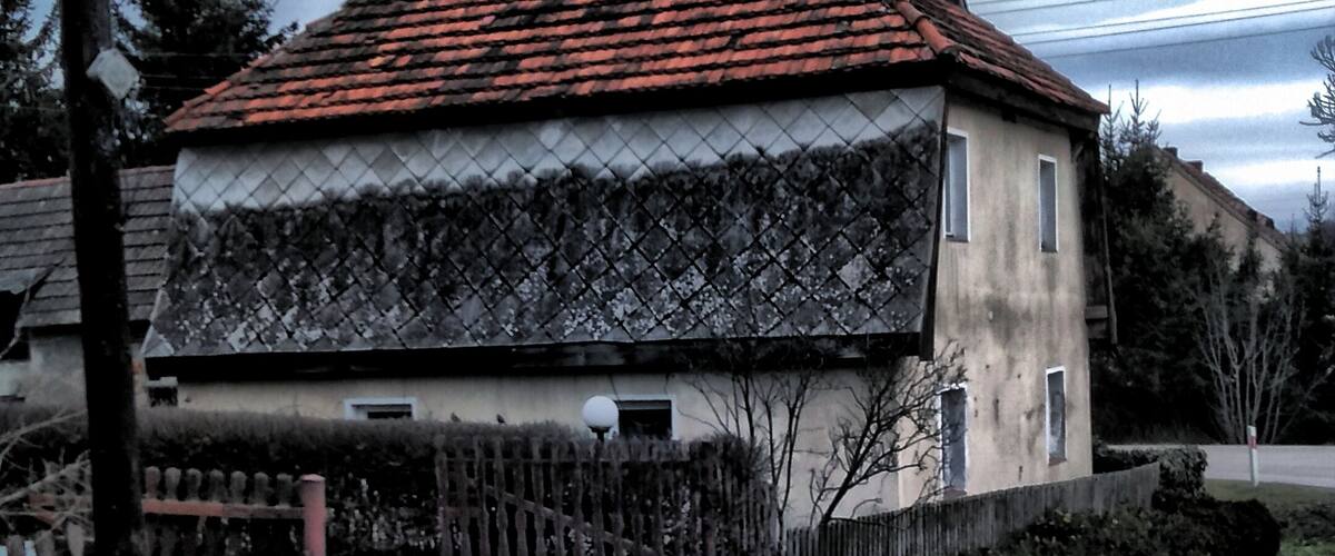 A house with a red-tiled roof, a stone wall, and a paved driveway.