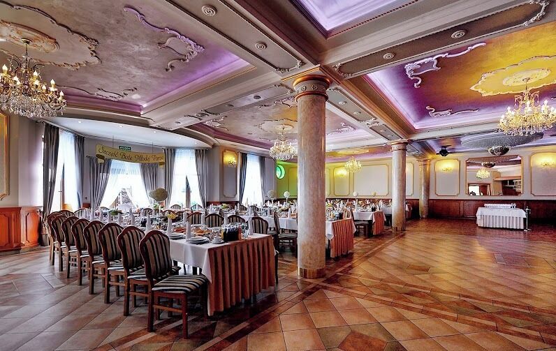 A banquet hall with wooden floors, round tables, and chairs.