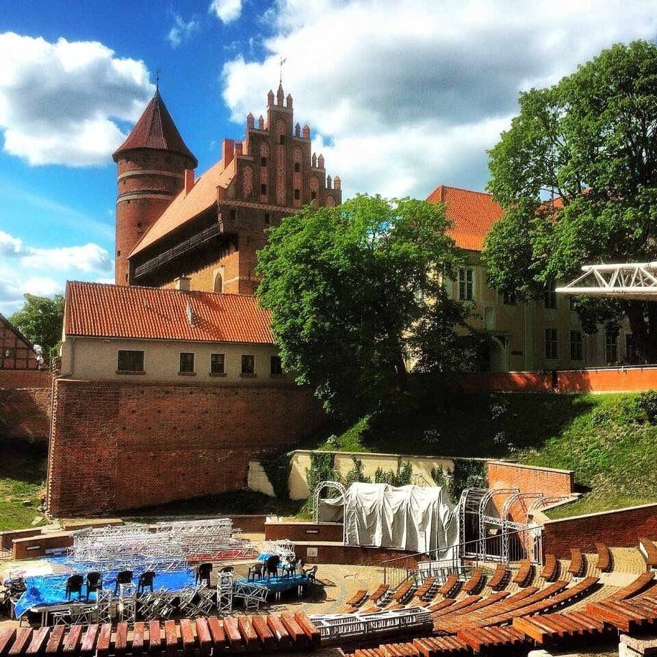 A historic castle with a prominent tower, a large courtyard with a stage, and a surrounding brick wall.