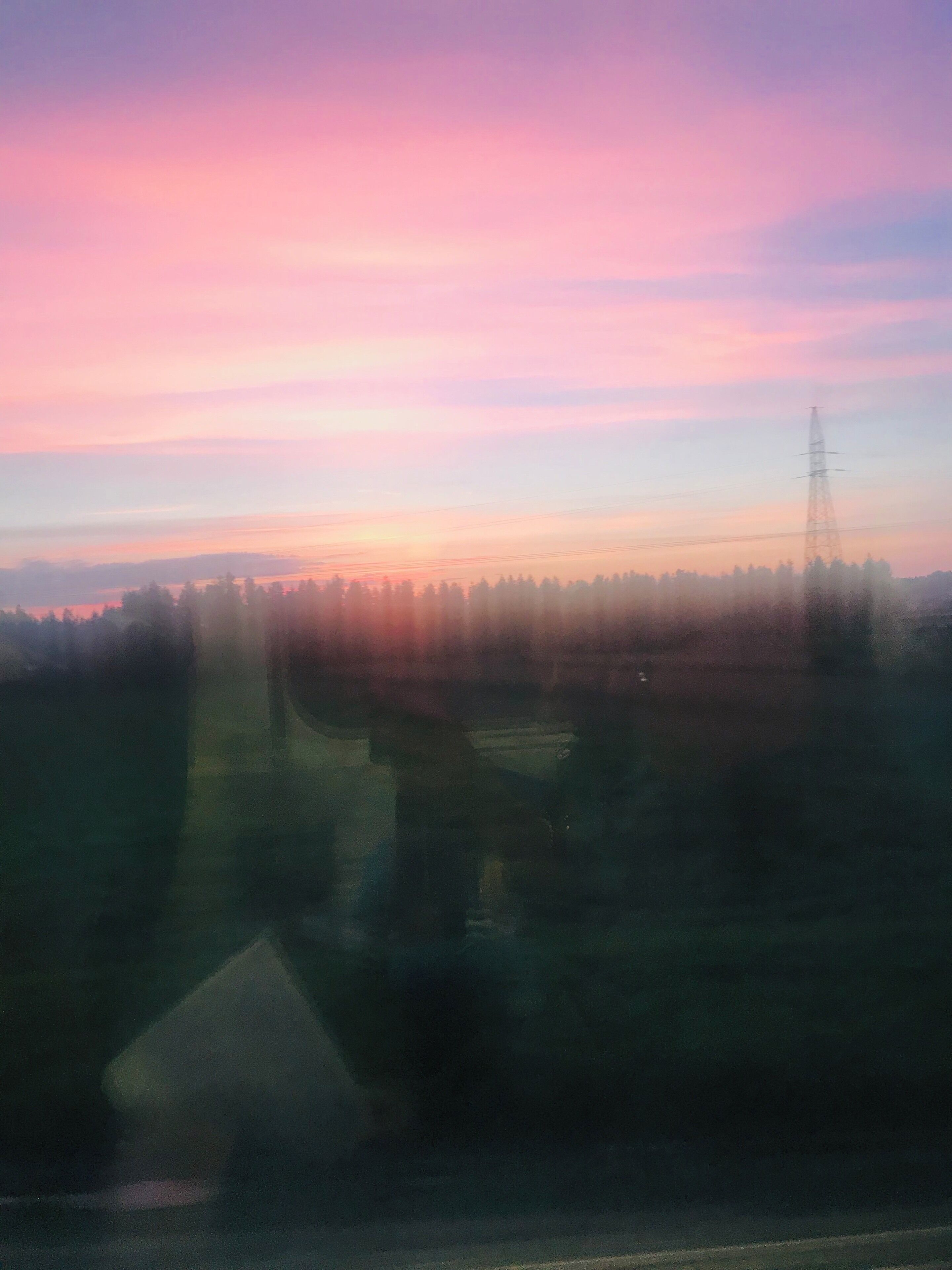 A sunset over a forested landscape with a power line tower.