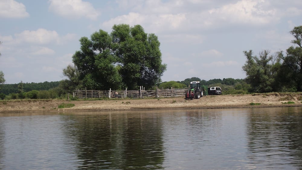 Ein ruhiger Fluss mit einer Holzzahlung und einem Traktor in der Nähe des Ufers.