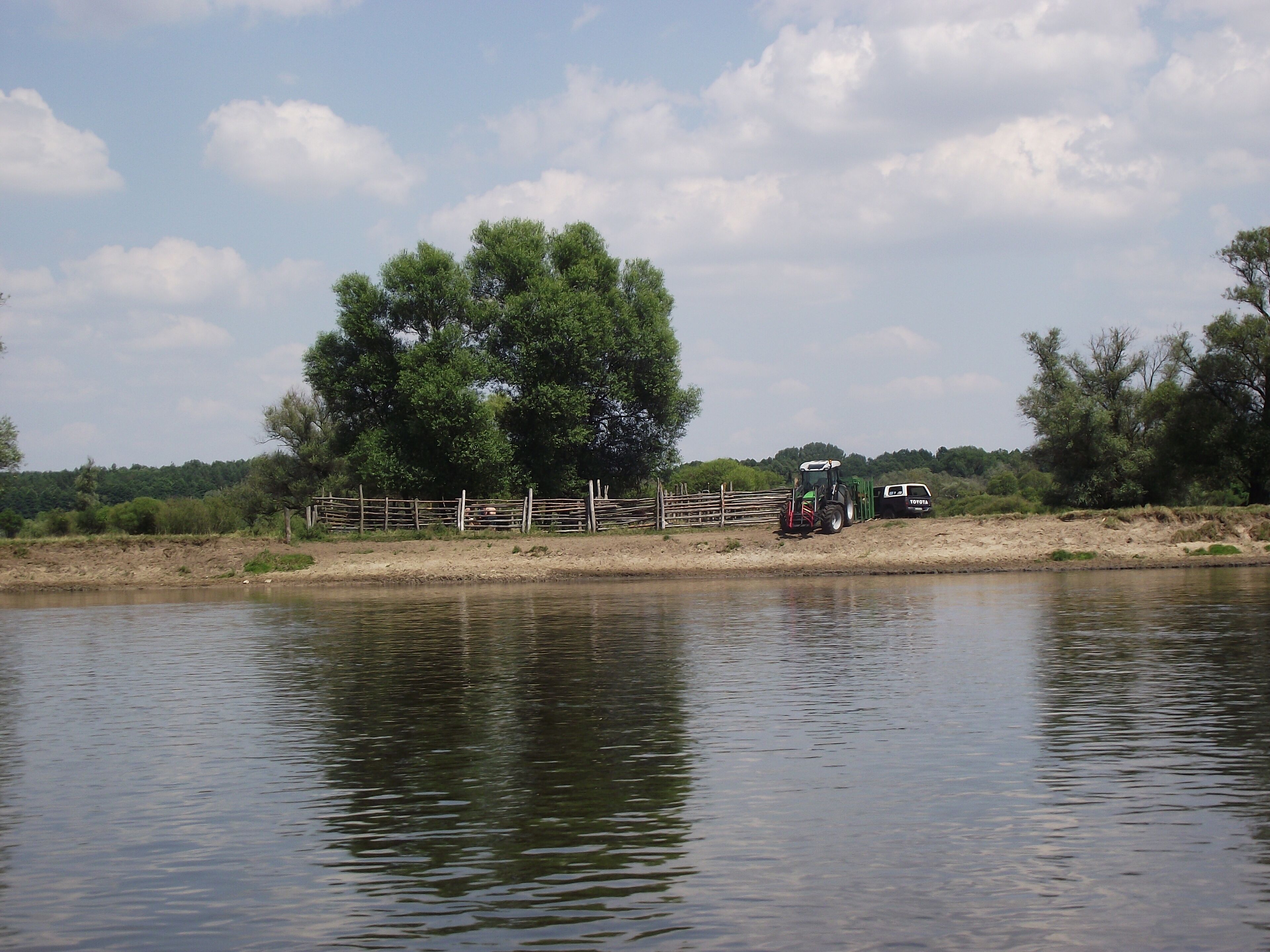 A calm river with a wooden fence and a tractor near the bank.