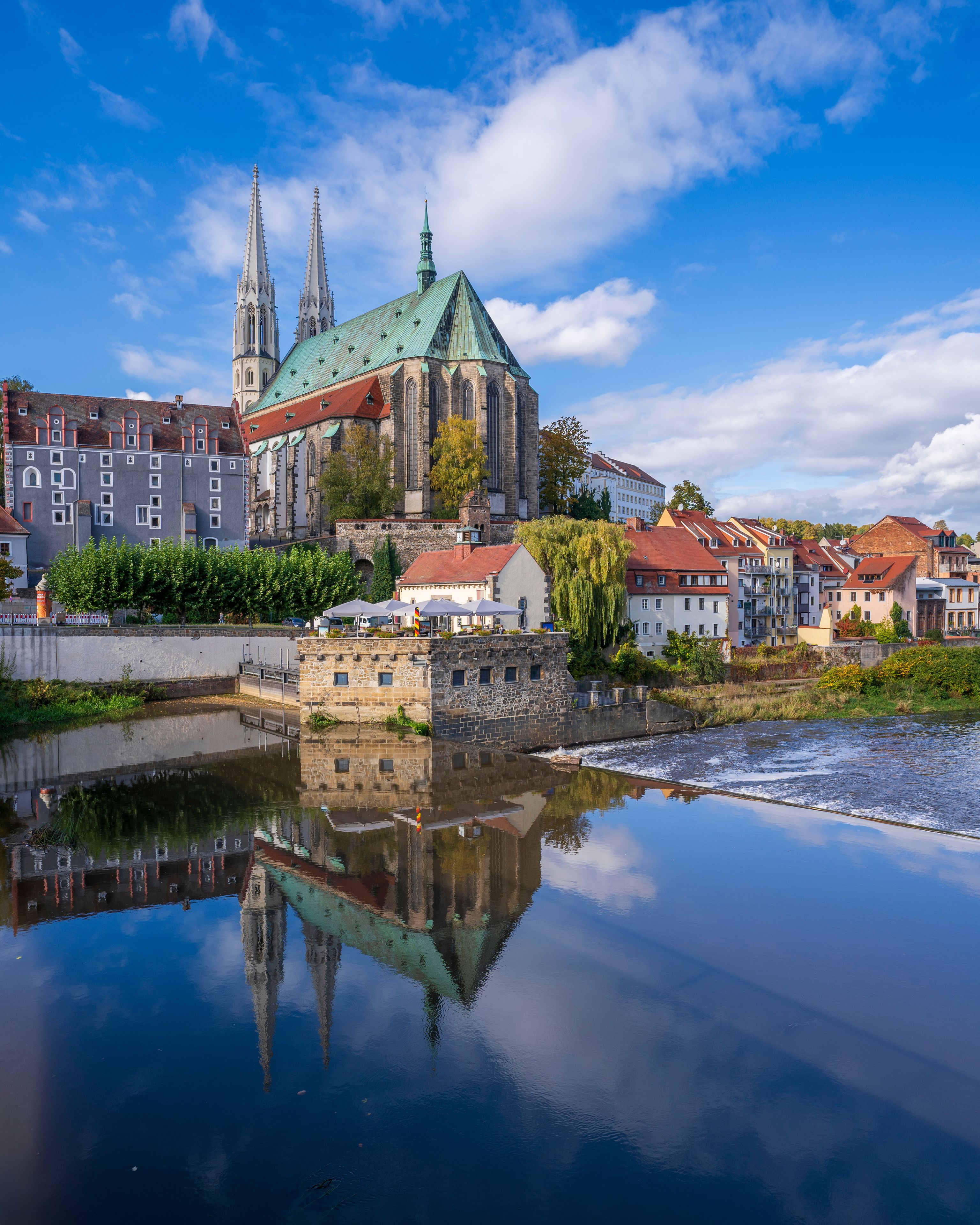 A historic church with twin spires, a river reflecting its architecture, and surrounding residential buildings.