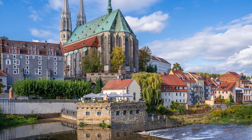 A historic church with twin spires, a river reflecting its architecture, and surrounding residential buildings.