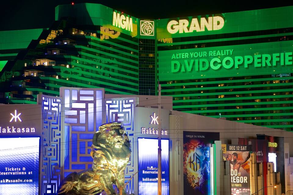 A night view of the MGM Grand hotel with illuminated signs and a statue in front.