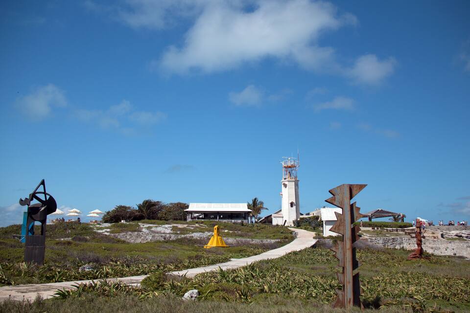 A coastal landscape with a lighthouse, a windmill, and a yellow buoy.