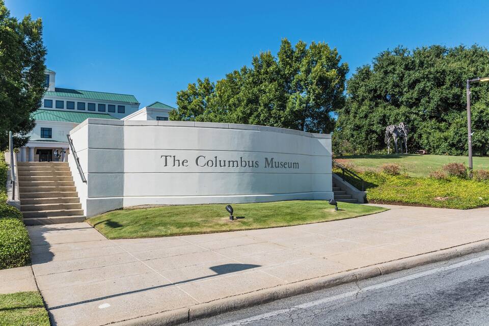 The Columbus Museum with a large sign, a grassy area, and a staircase leading to the entrance.