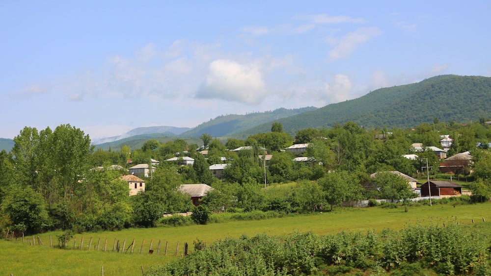 Un paysage rural caractérisé par des collines douces, des maisons éparpillées et un ciel dégagé.