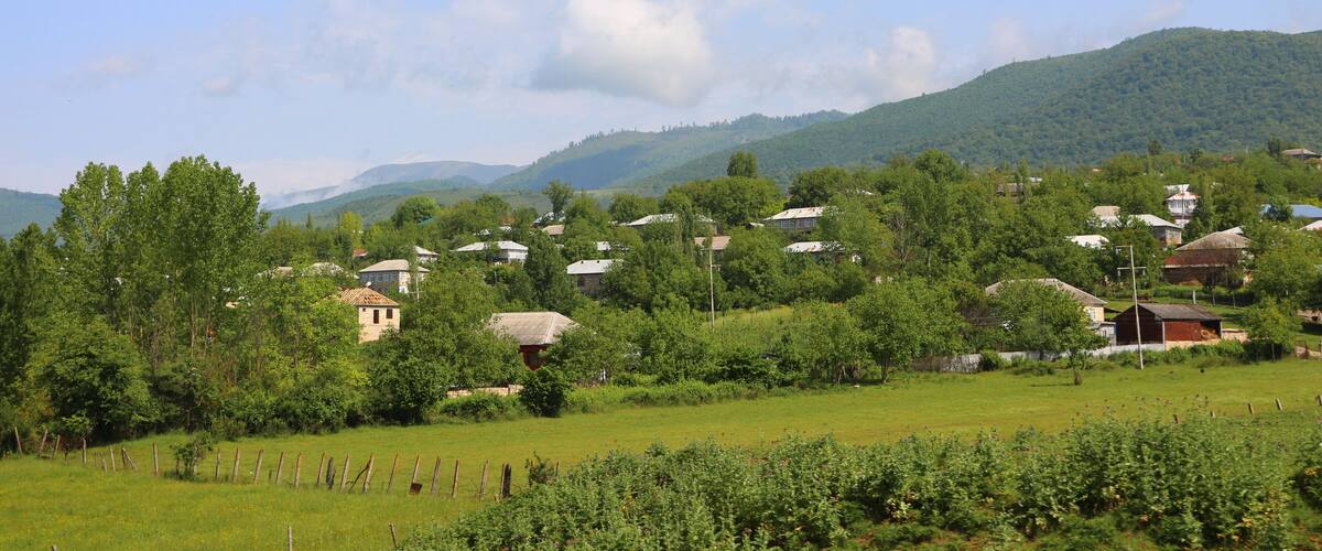 A rural landscape with rolling hills, scattered houses, and a clear sky.