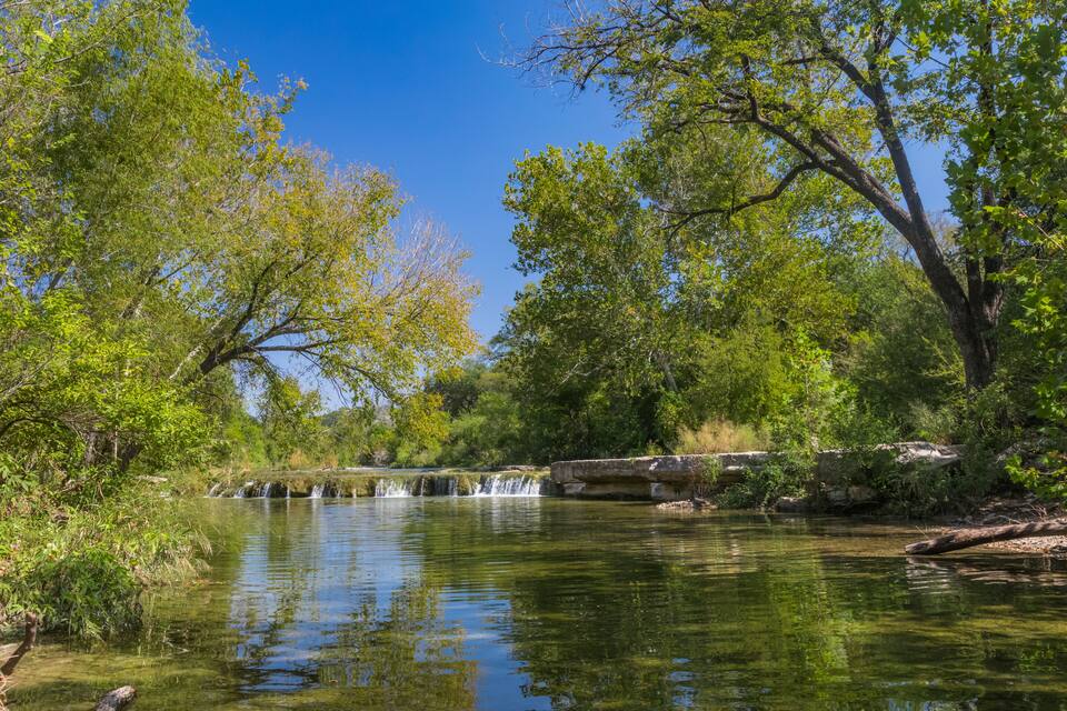 Un río tranquilo con una cascada, rodeado de abundante vegetación y árboles.