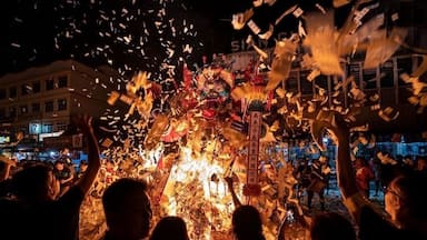 Celebração noturna com uma fogueira grande e pessoas jogando dinheiro para o alto.