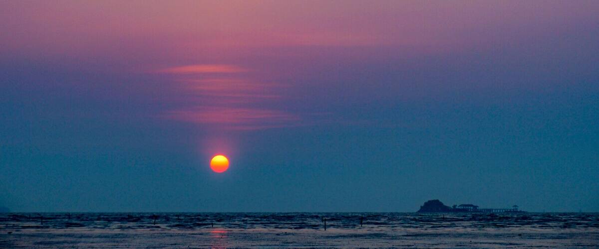 A sunset over the ocean with a small island in the distance.