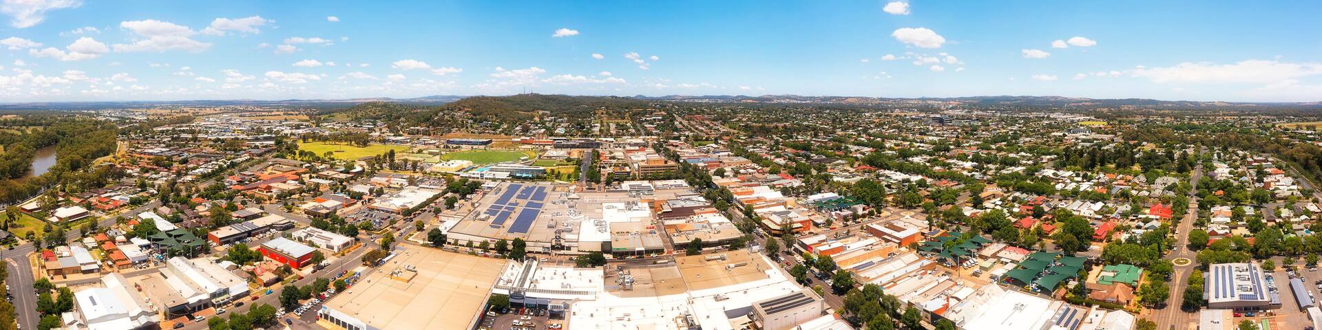 A panoramic view of a city with a river, green spaces, and a large industrial area with solar panels.