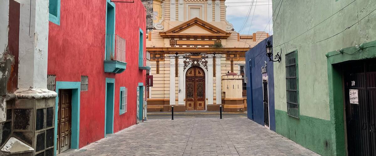 A narrow cobblestone street flanked by colorful buildings, leading to a historic church with a prominent entrance and a bell tower.
